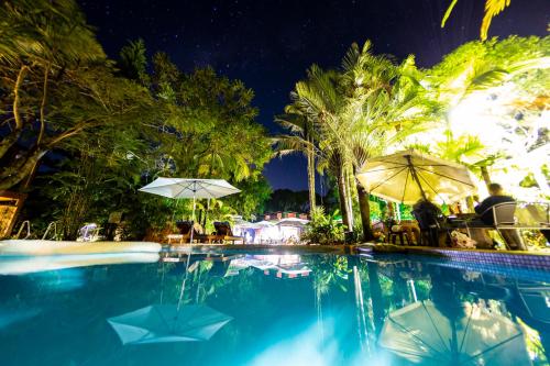 a swimming pool with people sitting under umbrellas at Dougies Backpackers Resort in Port Douglas