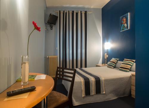 Cette petite chambre comprend un lit et une table avec un vase. dans l'établissement Logis Hotel Le Clos Des Oliviers, à Bourg-Saint-Andéol