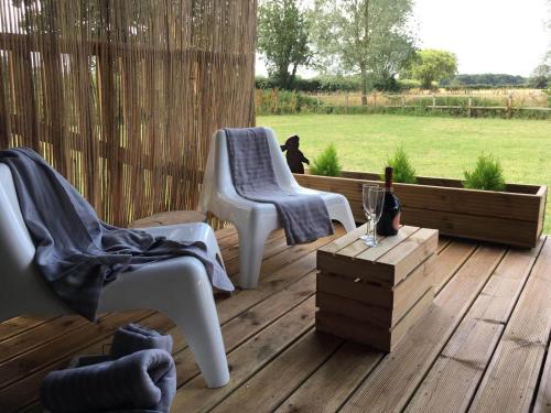 two white chairs on a wooden deck with a bottle of wine at Wingfield Escapes in Diss