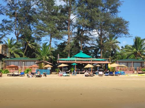 a beach with umbrellas and people sitting on the sand at Sea Front Beach Huts in Patnem