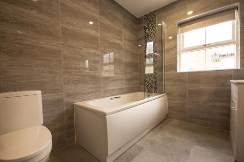 Un baño con bañera, inodoro y ventana. en Haddon Cottage - Darwin Lake Holiday Village, en Matlock