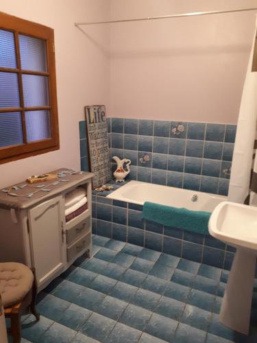 La salle de bains est pourvue de carrelage bleu, d'une baignoire et d'un lavabo. dans l'établissement Potter's Cottage, à Vindefontaine