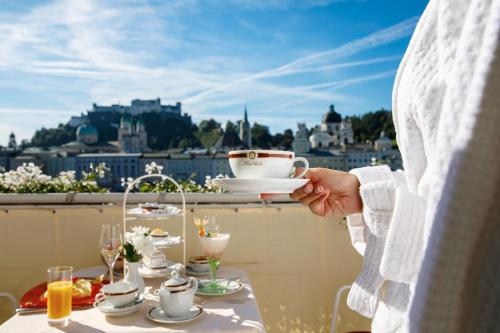 a person holding a tea cup on top of a balcony at Hotel Sacher Salzburg in Salzburg