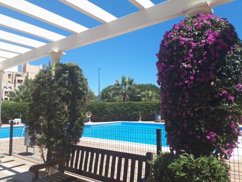 un banc sous une pergola fleurie à côté d'une piscine dans l'établissement Apartamento Playa Verde, à Isla Canela