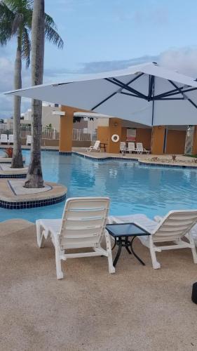 - une piscine avec 2 chaises et un parasol dans l'établissement Tropical Delightful Guest Studio, à Canovanas