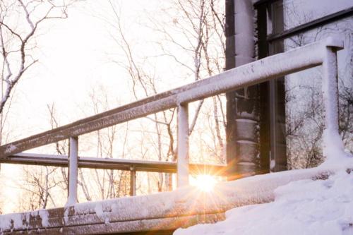 a snow covered railing with the sun shining through a window at Villa Váibmu in Inari