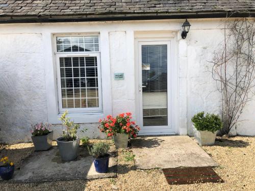a white house with potted plants in front of a door at GROOMS COTTAGE OUTSIDE HOT TUB in Beith