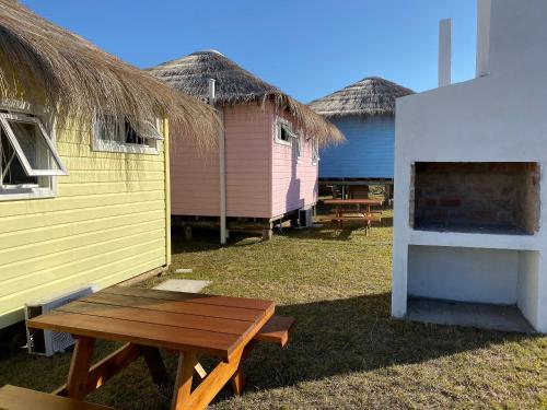a group of huts with a picnic table in the grass at Cabañas Punta Papaya in Punta Del Diablo
