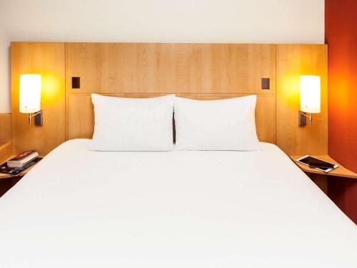 a large white bed in a hotel room with two lamps at ibis Lyon Est Chaponnay in Chaponnay