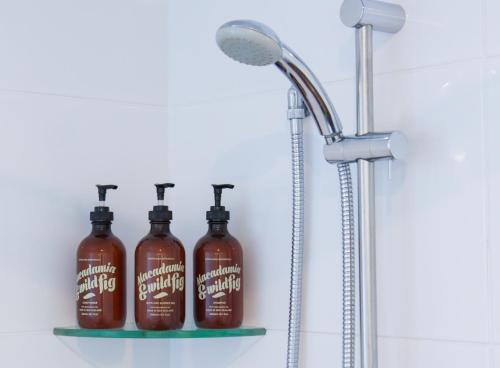 three bottles of shower cleaner on a shelf in a bathroom at 850 Cameron Motel in Tauranga