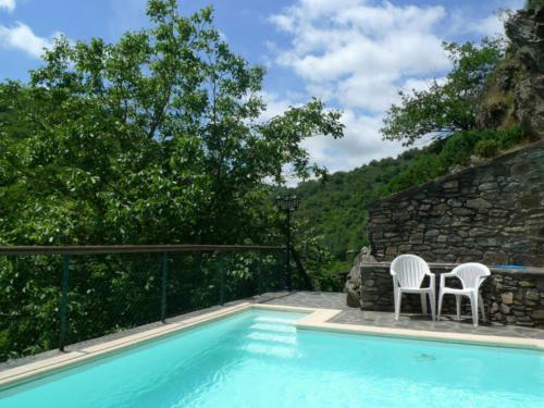 uma piscina com duas cadeiras brancas ao lado de uma parede de pedra em Le Four em Vieillevie