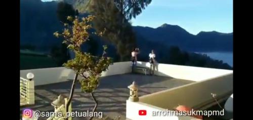 two people standing on top of a building with mountains in the background at Bromo Otix Guest House in Bromo