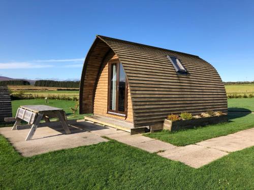 a small wooden cabin with a table in the grass at Loch Shin Glamping Pods in Lairg