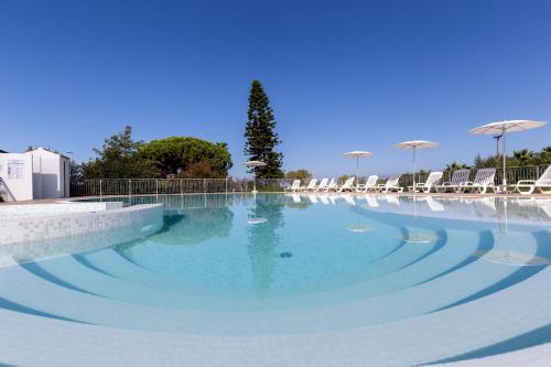 a large pool of blue water with chairs and umbrellas at Happy Days in Capo Vaticano