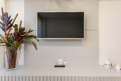a flat screen tv on a white wall with a plant at Apartamento NOVO - Beira mar de Intermares in Cabedelo