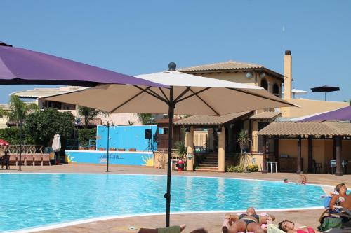 a group of people sitting around a swimming pool with an umbrella at Campofelice Holidays in Campofelice di Roccella