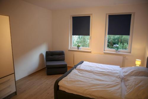 a bedroom with a bed and a chair and two windows at FeWo Bergblick in Osterode