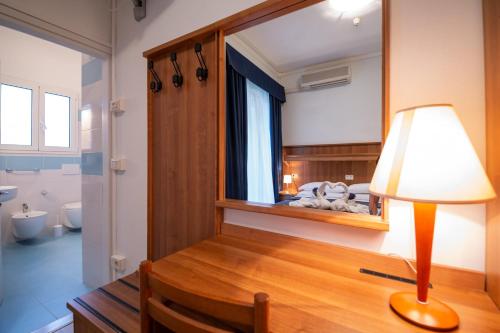 Habitación con escritorio, lámpara y espejo. en Hotel Mimosa, en Lignano Sabbiadoro