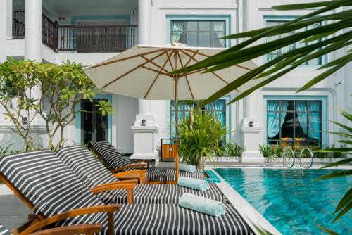 a swimming pool with lounge chairs and an umbrella at Anio Boutique Hotel Hoian in Hoi An