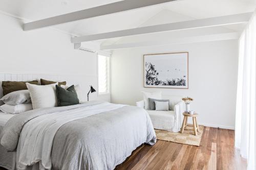 a white bedroom with a bed and a chair at Cape Beach House in Byron Bay