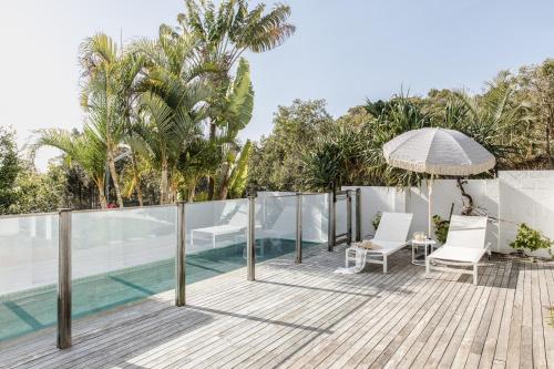 an outdoor deck with chairs and an umbrella next to a swimming pool at Cape Beach House in Byron Bay