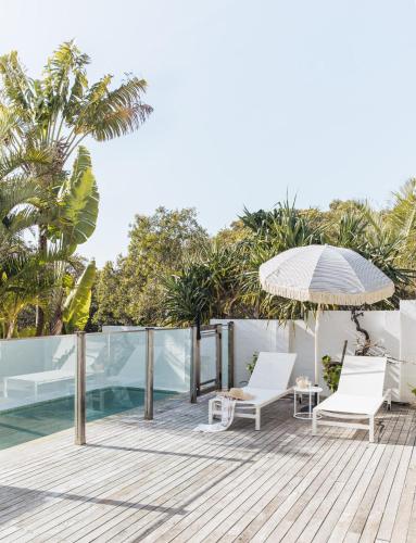 an outdoor deck with two chairs and an umbrella at Cape Beach House in Byron Bay