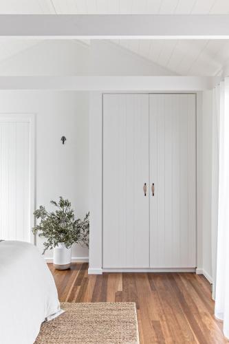 a bedroom with white walls and a bed with a closet at Cape Beach House in Byron Bay