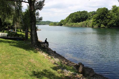 a man is sitting on a bench fishing on a lake at Maison Lac de Pareloup -LES PIEDS DANS L'EAU- in Arvieu