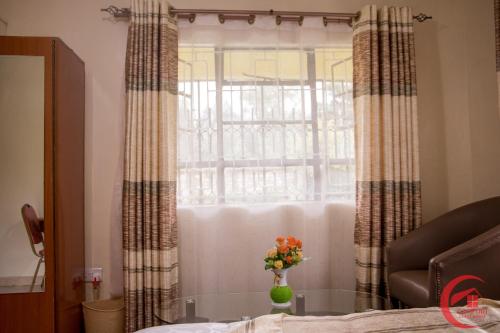 a vase of flowers on a glass table in front of a window at Comfort Guest House in Kericho