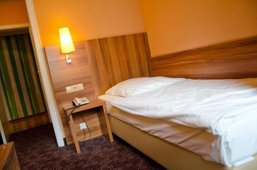 a bedroom with a bed and a night stand with a phone at Rheinland Hotel in Bonn