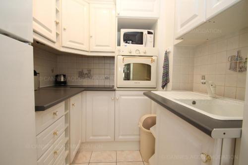 une cuisine blanche avec un évier et un micro-ondes dans l'établissement Jonquille, à Cannes