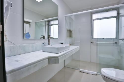 a white bathroom with a sink and a mirror at Wyndham Golden Foz Suítes in Foz do Iguaçu