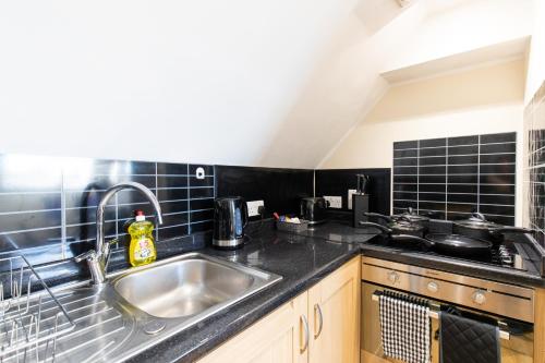 uma cozinha com um lavatório de aço inoxidável e azulejos pretos em Velvet 2-bedroom apartment, Clockhouse, Hoddesdon em Hoddesdon