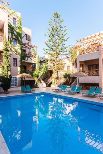 a swimming pool at a hotel with chairs and trees at Anna Maria in Malia