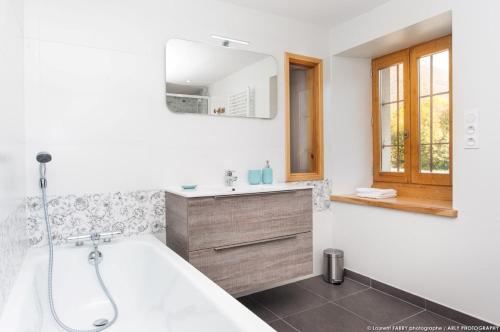 La salle de bains est pourvue d'une baignoire, d'un lavabo et d'un miroir. dans l'établissement GÎTE DU PORCHE, à Saint-Jean-de-la-Porte