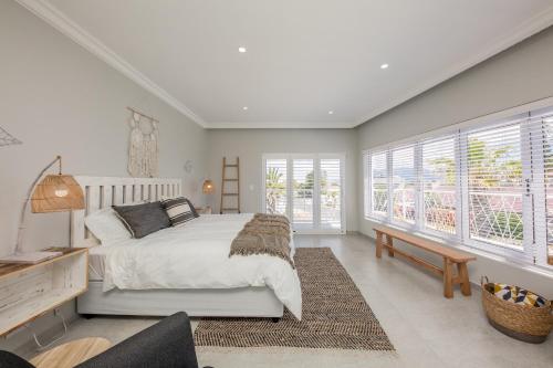 a bedroom with a bed and a desk and windows at The Little Palm in Bloubergstrand