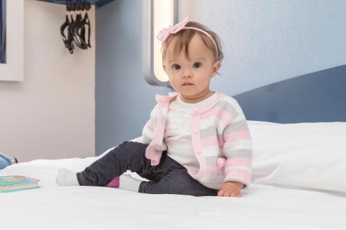 a little girl sitting on a bed at ibis budget Curitiba Centro in Curitiba