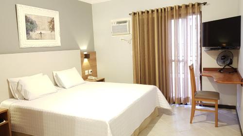 um quarto de hotel com uma cama branca e uma secretária em Hotel Central Parque em São Lourenço