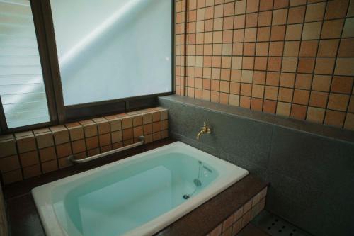 a bath tub in a tiled bathroom with a window at Ochiairo in Izu