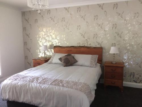 a bedroom with a bed with white sheets and birds on the wall at Kymmik Cottage in Geeveston