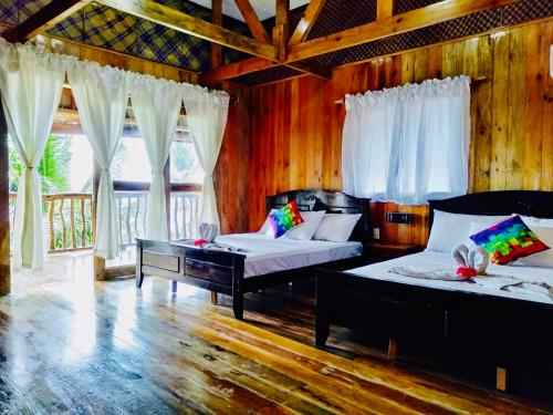 two beds in a room with wooden walls and windows at White Beach Front and Cottages in Buruanga