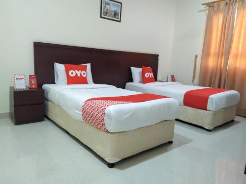 2 camas en una habitación de hotel con almohadas rojas y blancas en Super OYO 107 Al Areen Hotel Apartments, en Shāhiq