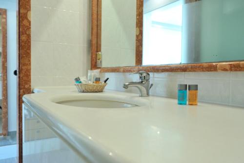 a bathroom sink with a mirror and a basket of toothbrushes at Possidi Holidays Resort & Suite Hotel in Possidi