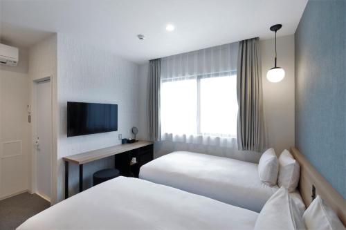 a hotel room with two beds and a desk and a television at M's Hotel Sanjo Omiya in Kyoto