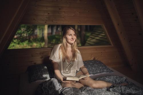 a girl sitting on a bed reading a book at Forest Camping Mozirje in Mozirje