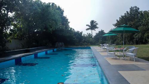 a pool with tables and chairs and an umbrella at Jungle Safari Resort & Holiday Villa in Nashik