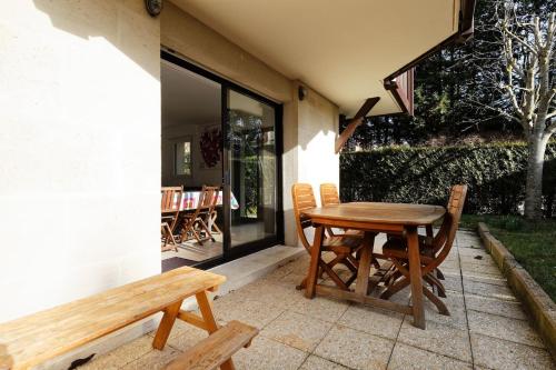 une table et des chaises en bois sur une terrasse avec un banc dans l'établissement Charmant 3 pièces avec jardin à 5mn de la plage, à Deauville