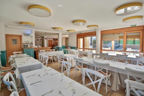un restaurante con mesas y sillas blancas y ventanas en La Posada de Ojebar Nórdica, en Rasines