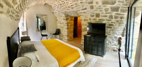 a bedroom with a bed and a tv in a stone wall at La Maison des Vendangeurs - TABLE D'HÔTES le soir du jeudi au dimanche- Jacuzzi - Balnéo SPA - ACCES PISCINE pour toutes les chambres sauf STUDIO COQUET- Piscine de mai à mi-octobre in Martignargues
