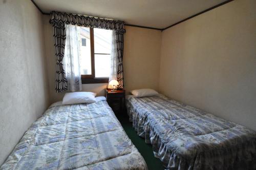 two beds in a room with a window at Guest House Wind Inn Hakuba in Hakuba